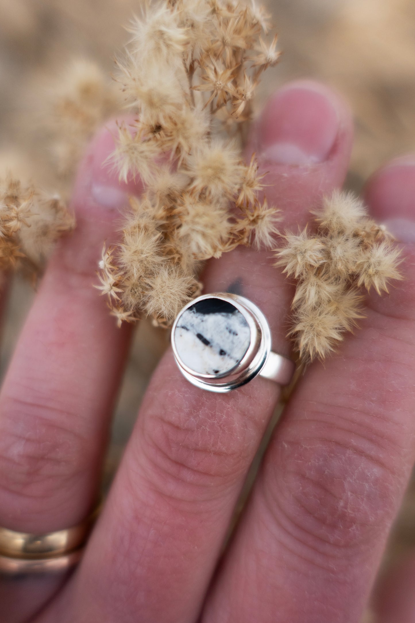 A hand holding a silver ring with a round white buffalo turquoise stone.