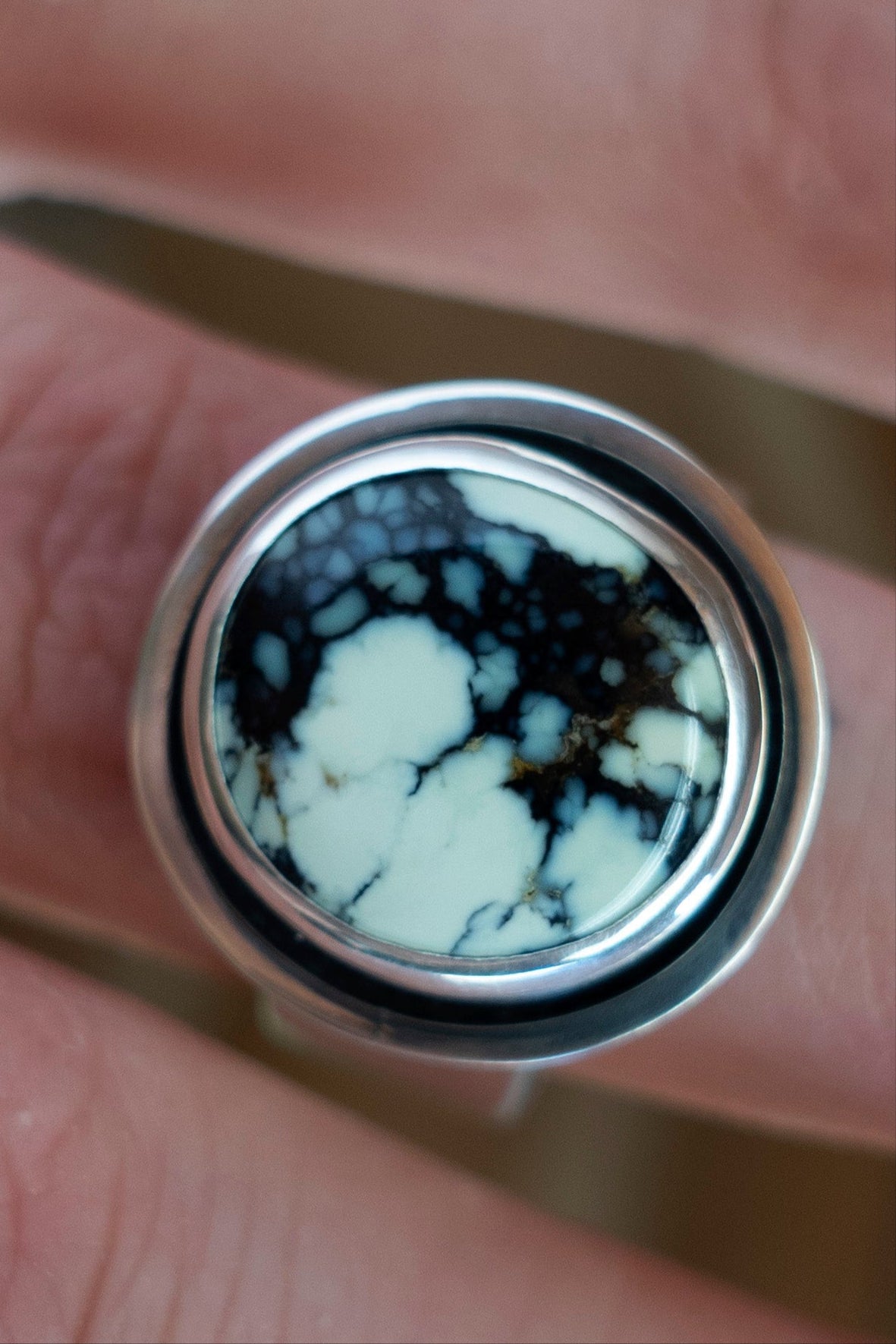 Close-up of a handmade Poseidon variscite sterling silver ring with a minty green stone with unique natural black matrix and a wide band being held between fingers.