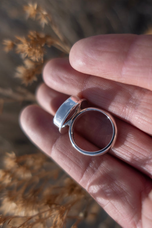 Profile view of a high quality, finely crafted sterling silver ring held in a hand against an earthy soft background.