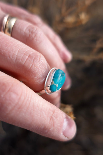 Finely polished shiny sterling silver ring with a vivid blue Kingman Turquoise cabochon worn on a hand photographed against a soft background