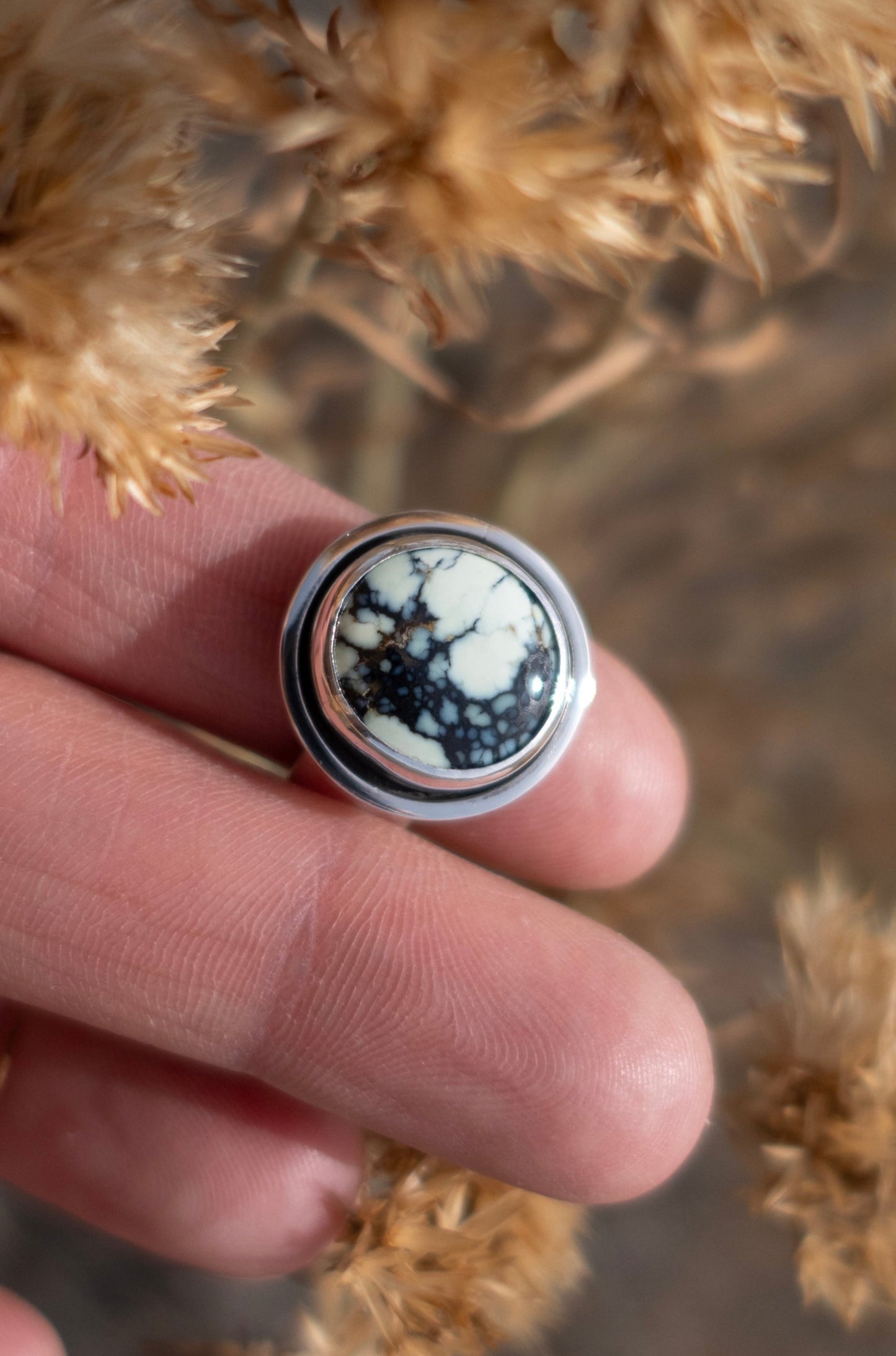 A beautiful handmade Poseidon Variscite sterling silver ring held by fingers surrounded by dried plants and a soft earthy background. Sunshine glints off the shiny polished silver.