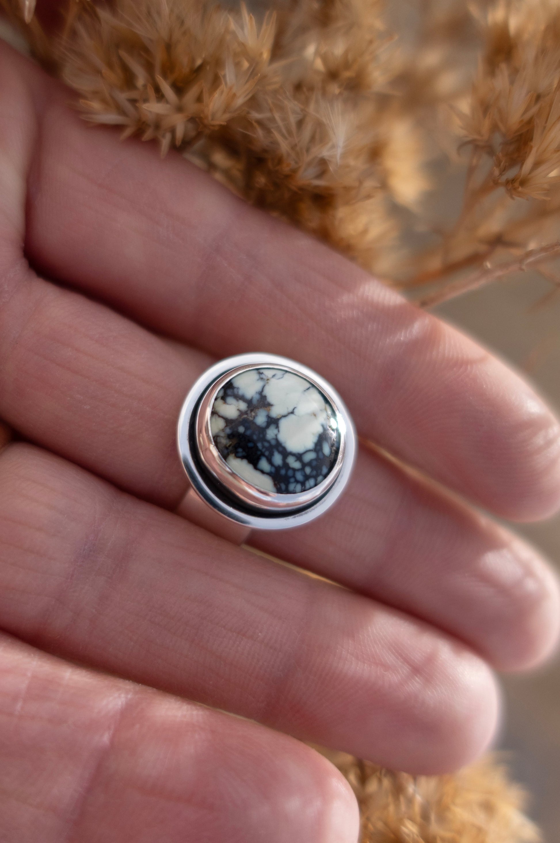 Silver ring with a circular Poseidon variscite cabochon in a shadowbox design held in a hand against a natural background