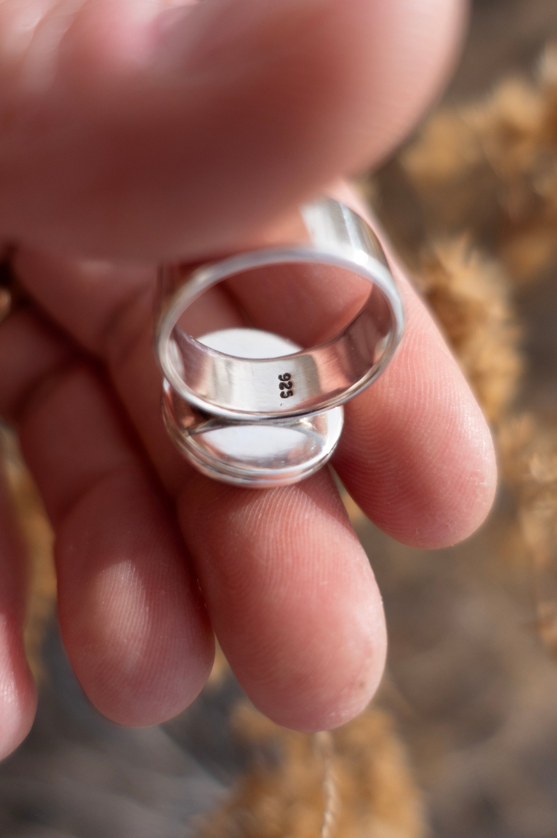 The inside of a well made sterling silver ring band stamped .925 (sterling silver) being held in a hand with a soft earthy background 
