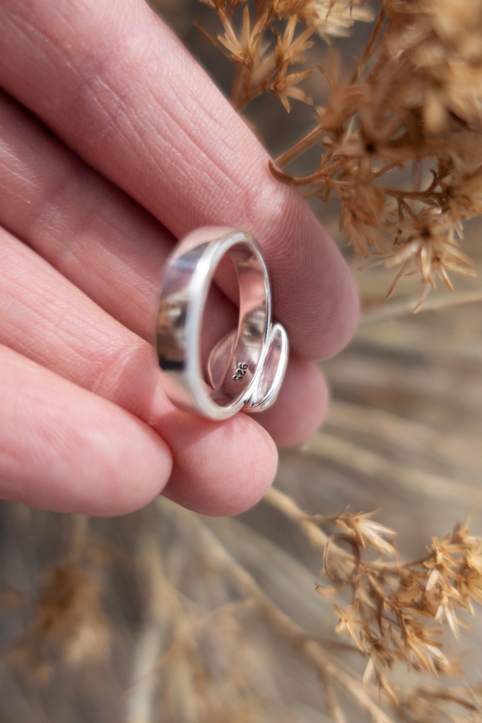 Silver ring held between fingers with a blurred natural background