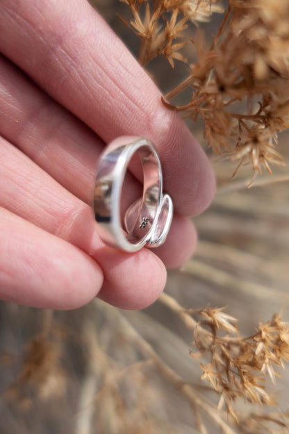 Silver ring held between fingers with a blurred natural background