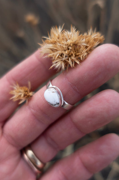 Hand holding a dried plant with a ring featuring a white stone.