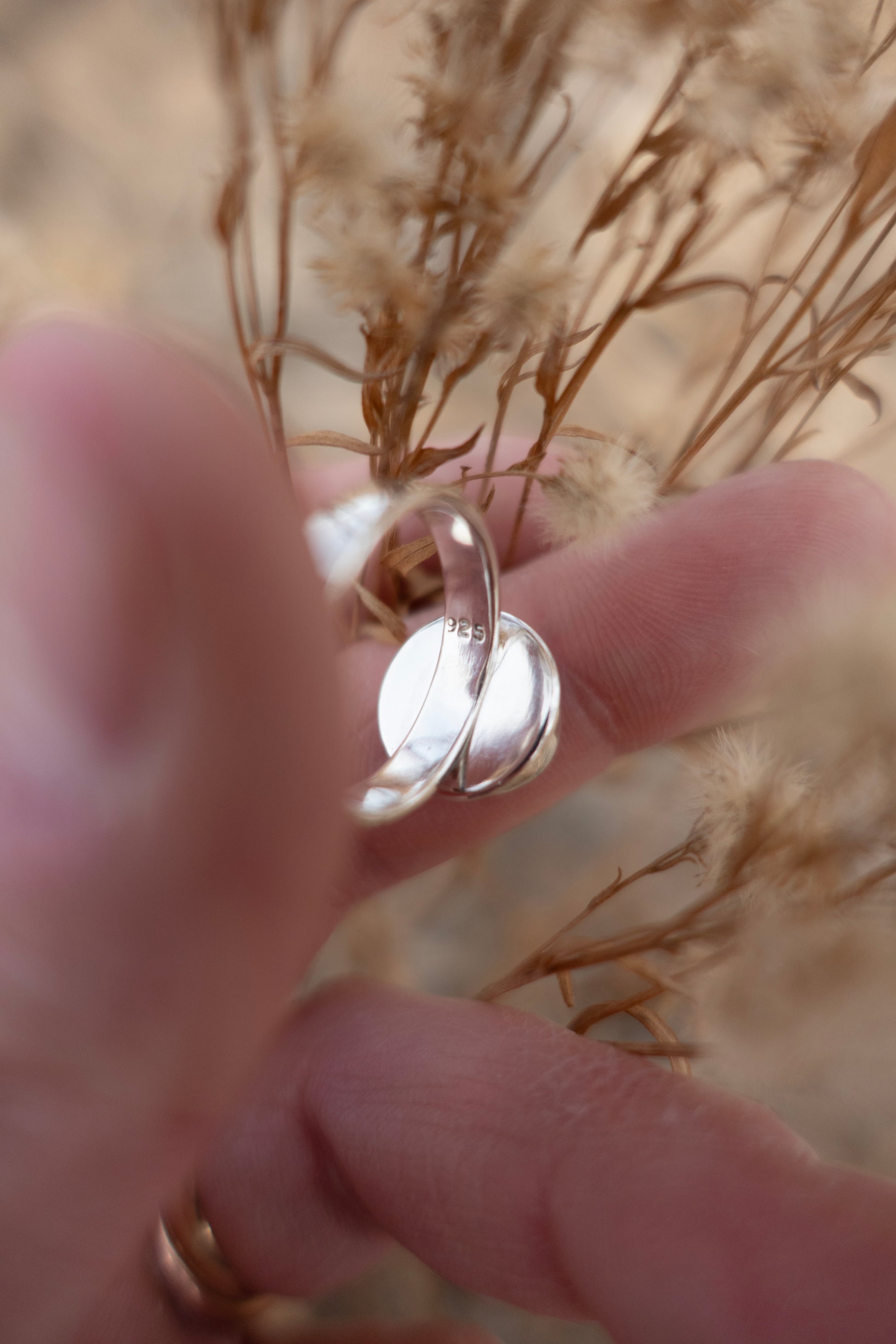 The inside of a sterling silver ring stamped .925 held in a hand surrounded by dried earthy florals