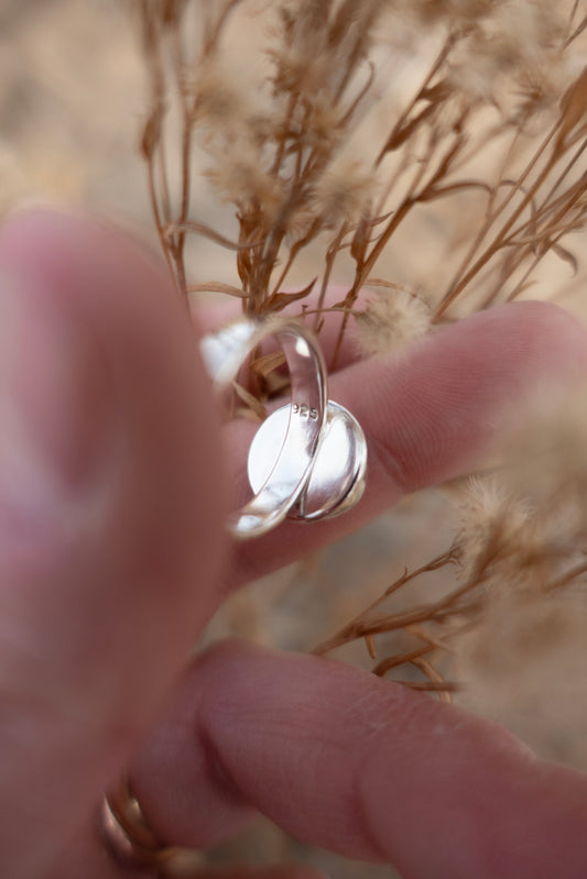 The inside of a sterling silver ring stamped .925 held in a hand surrounded by dried earthy florals