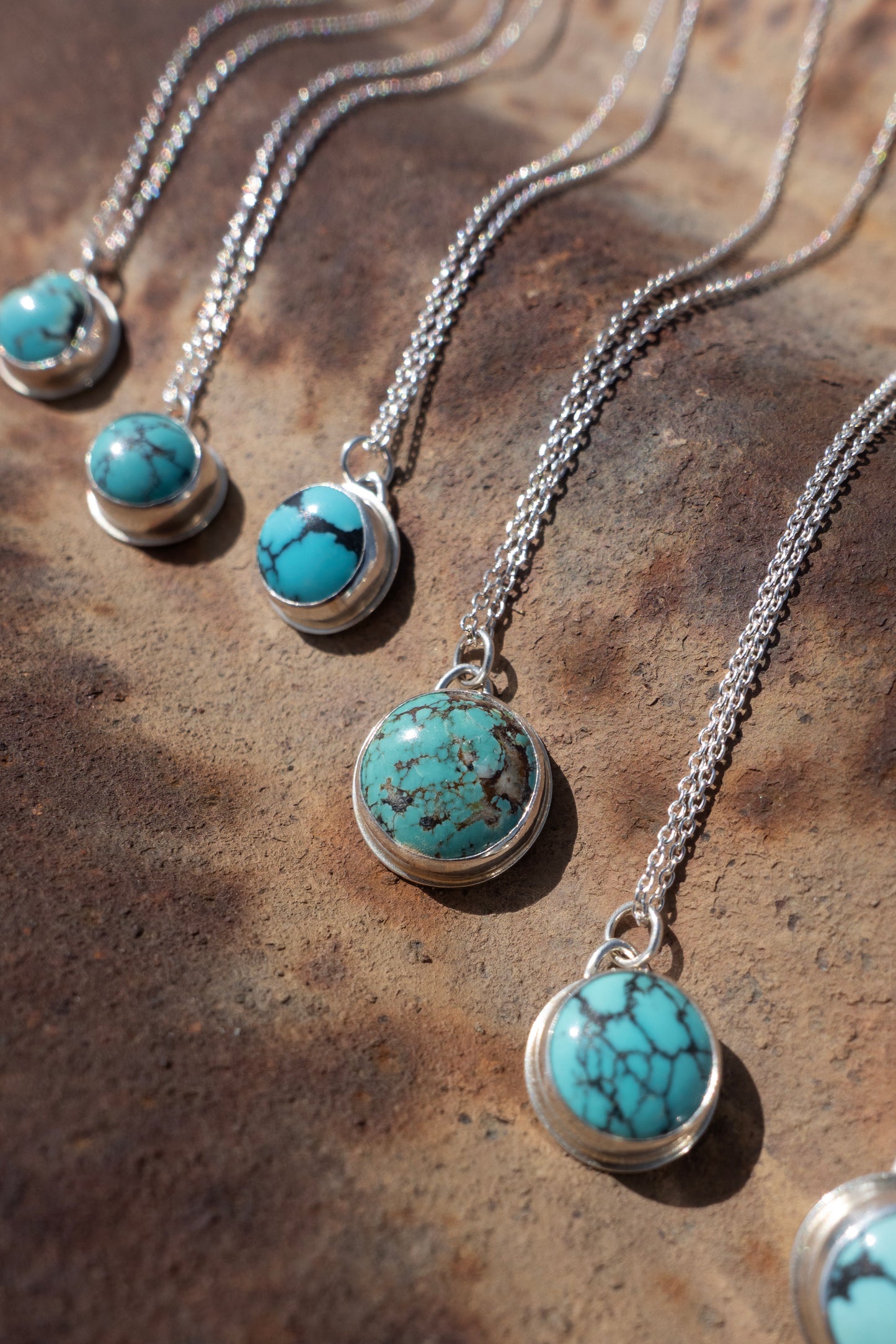 Kingman Turquoise charm necklaces with sterling silver chains on display against a rustic background