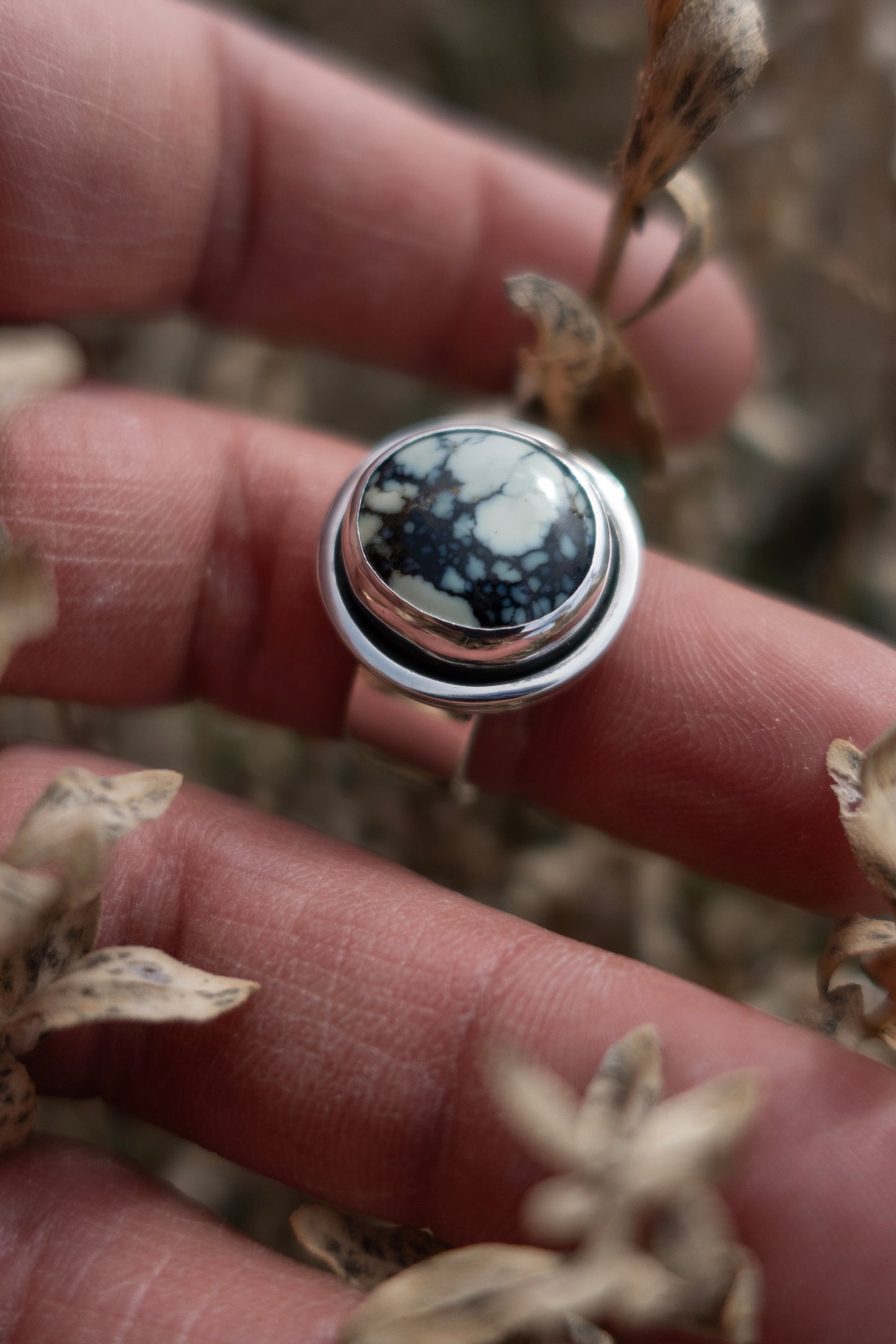A handmade poseidon variscite ring in a shadowbox sterling silver setting being held by a hand among dried vegetation.