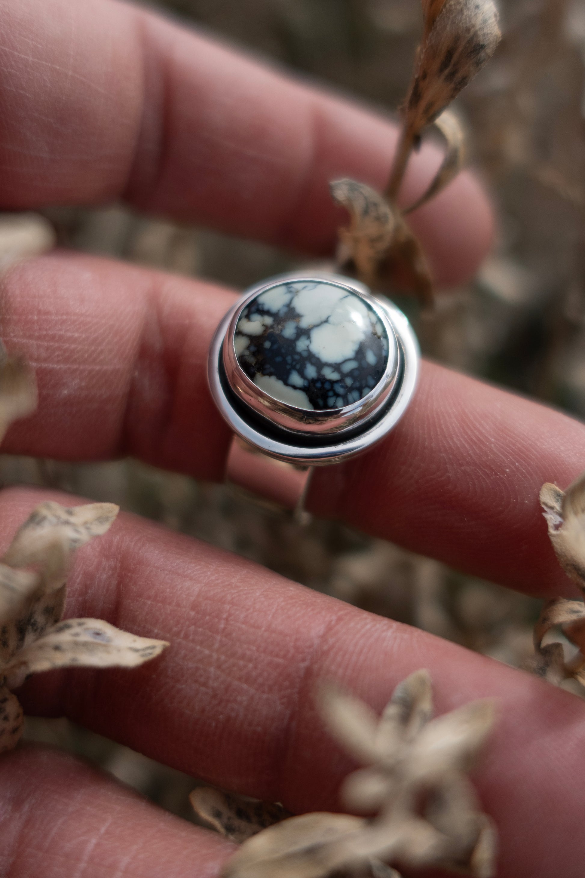 A handmade poseidon variscite ring in a shadowbox sterling silver setting being held by a hand among dried vegetation.
