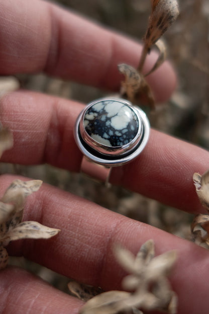 A handmade poseidon variscite ring in a shadowbox sterling silver setting being held by a hand among dried vegetation.
