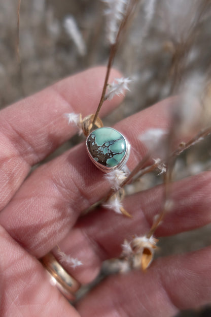 Sterling silver and green Damele Turquoise ring held in a hand surrounded by fuzzy white dried florals